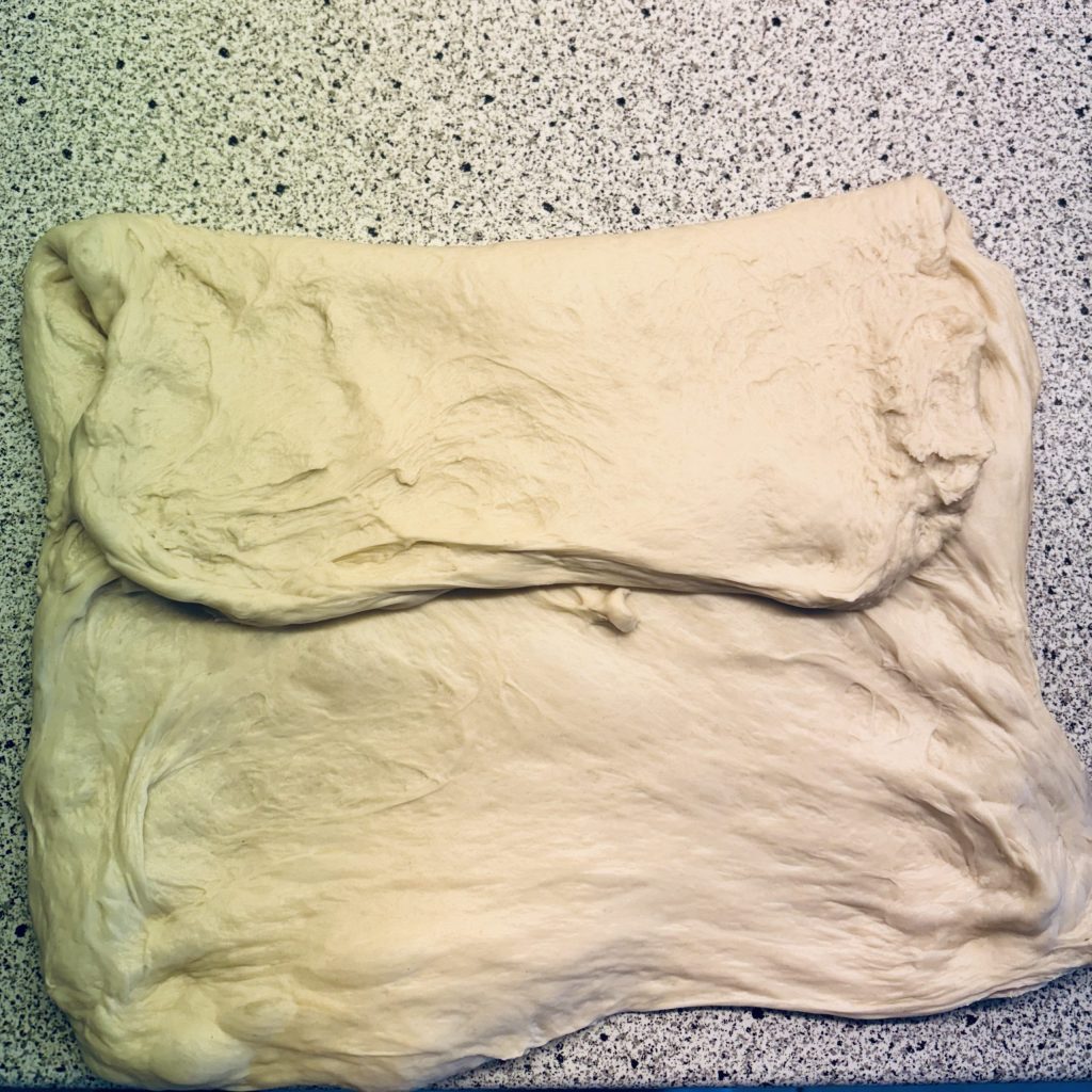 Ein flacher, elastischer Brotteig auf einer küchenarbeitsfläche aus Marmor, bereit zum Formen.