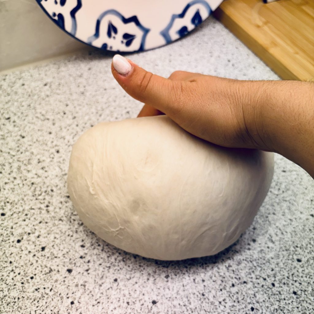 Eine Hand, die einen geformten Teigball hält, auf einer hellen Arbeitsfläche.