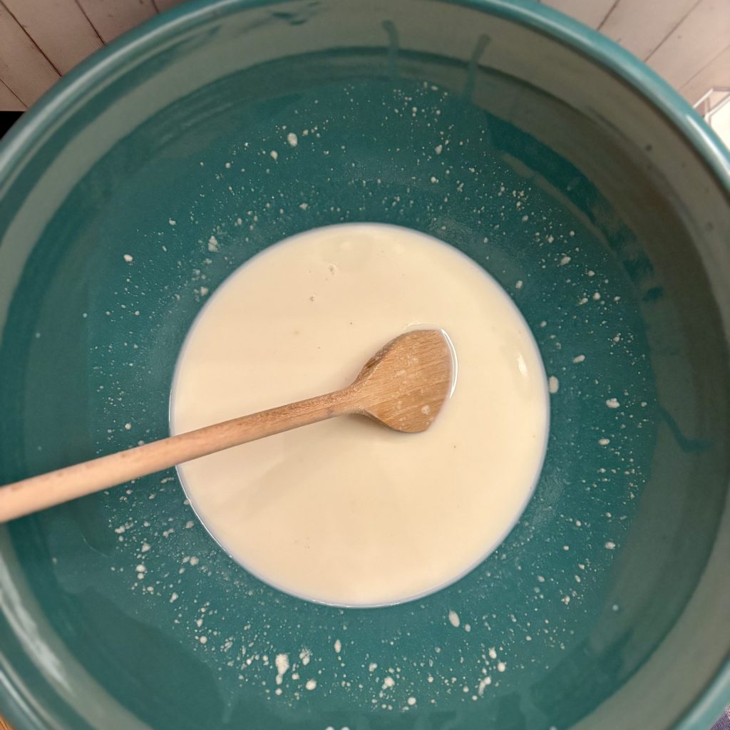 Eine Schüssel mit einer cremigen, hellen Flüssigkeit und einem Holzlöffel, der darin liegt.