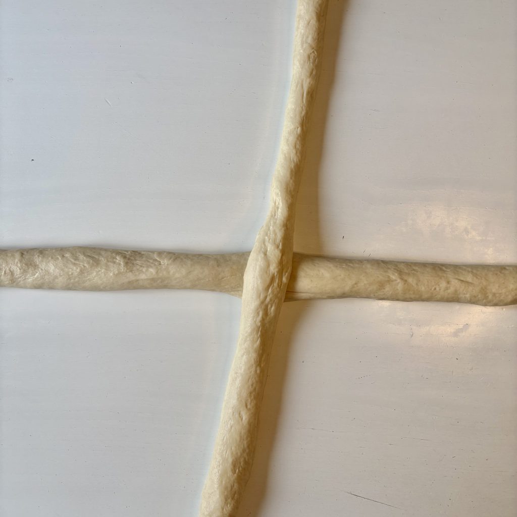 Two lengths of white felted wool lying in a cross shape on a light-colored surface