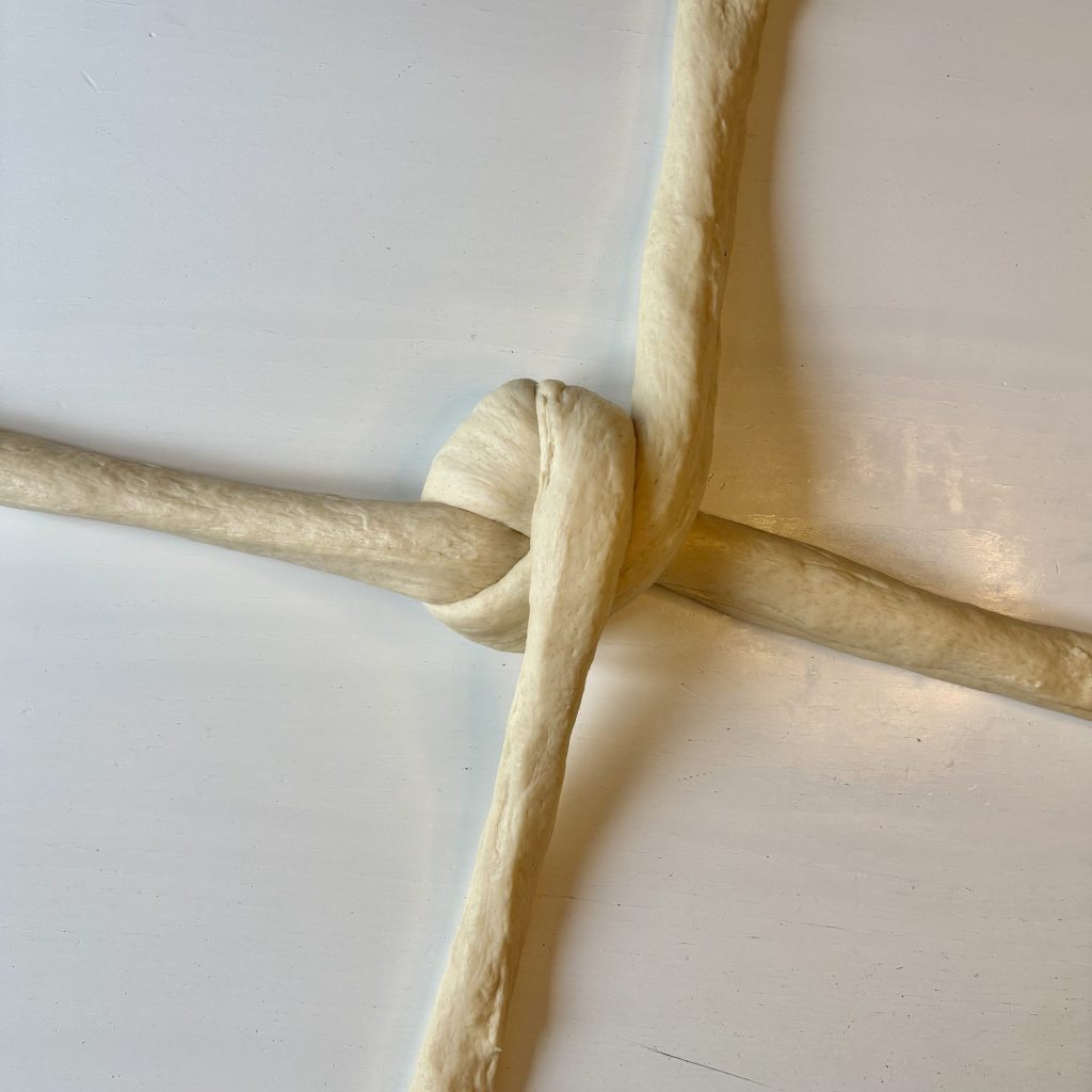 Close-up of a knot made from white fabric cords, positioned on a light-colored surface.