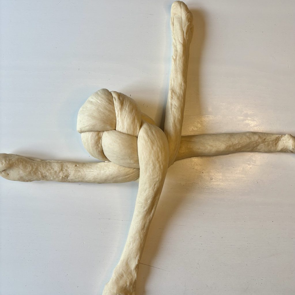 A knotted piece of dough arranged on a flat surface, resembling a cross shape with a braided section at the center.