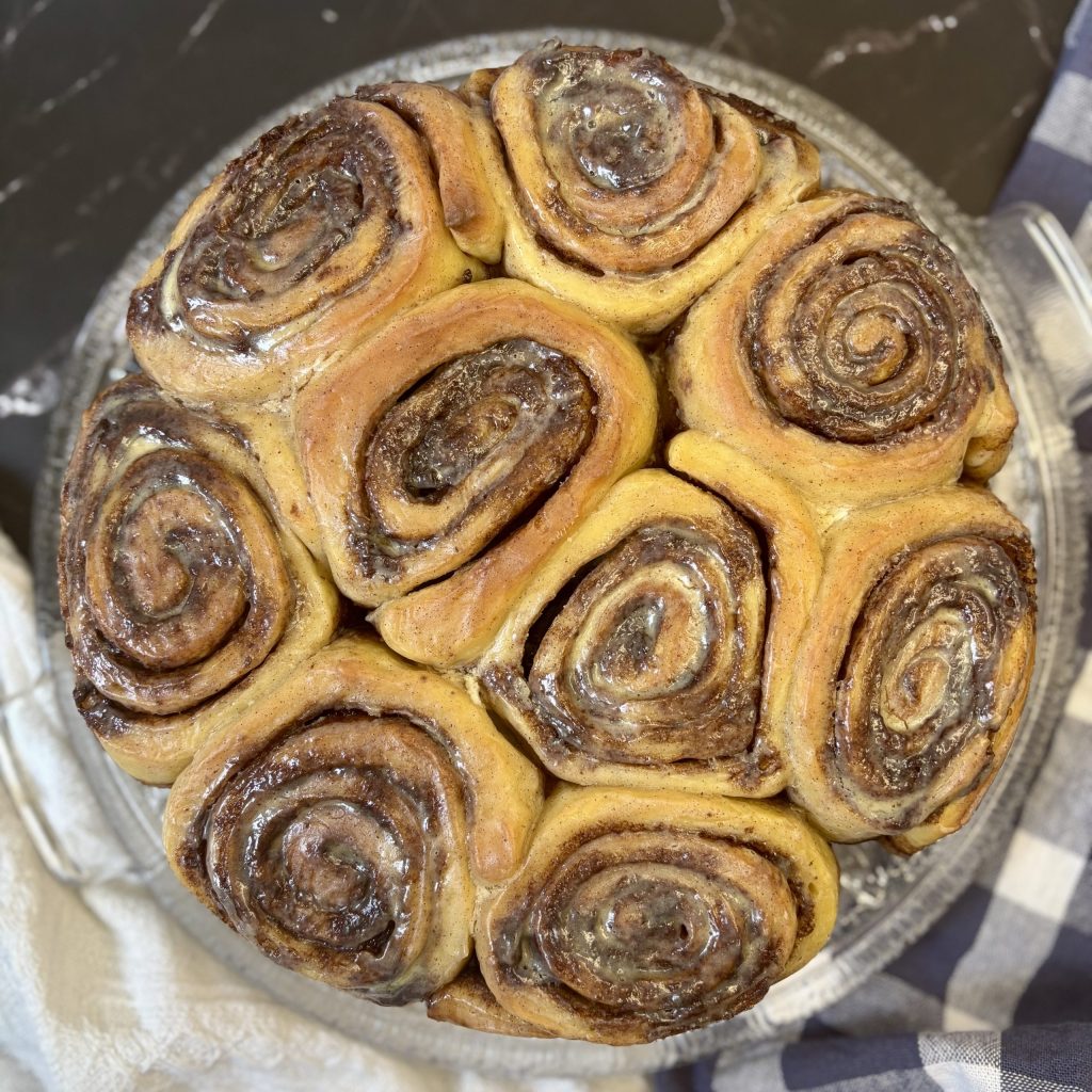 A top view of freshly baked cinnamon rolls arranged attractively in a round dish, showcasing their golden-brown color and spiral patterns.