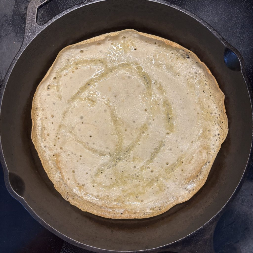 Sauerteigpizza-Boden, der in einer gusseisernen Pfanne vorgebacken wird, sichtbar mit goldbrauner Kruste.