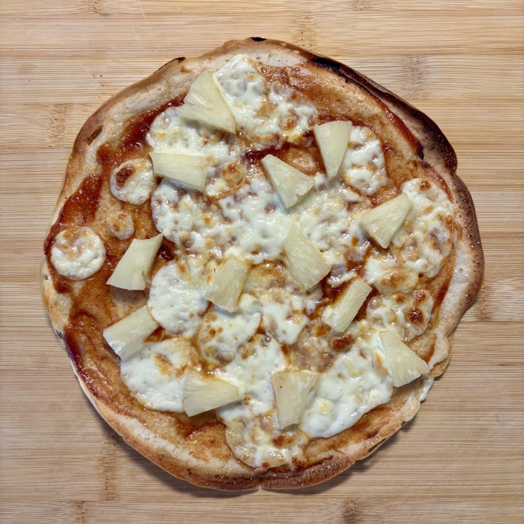 Hausgemachte Pizza mit Ananas und Käse auf einem Holzbrett.