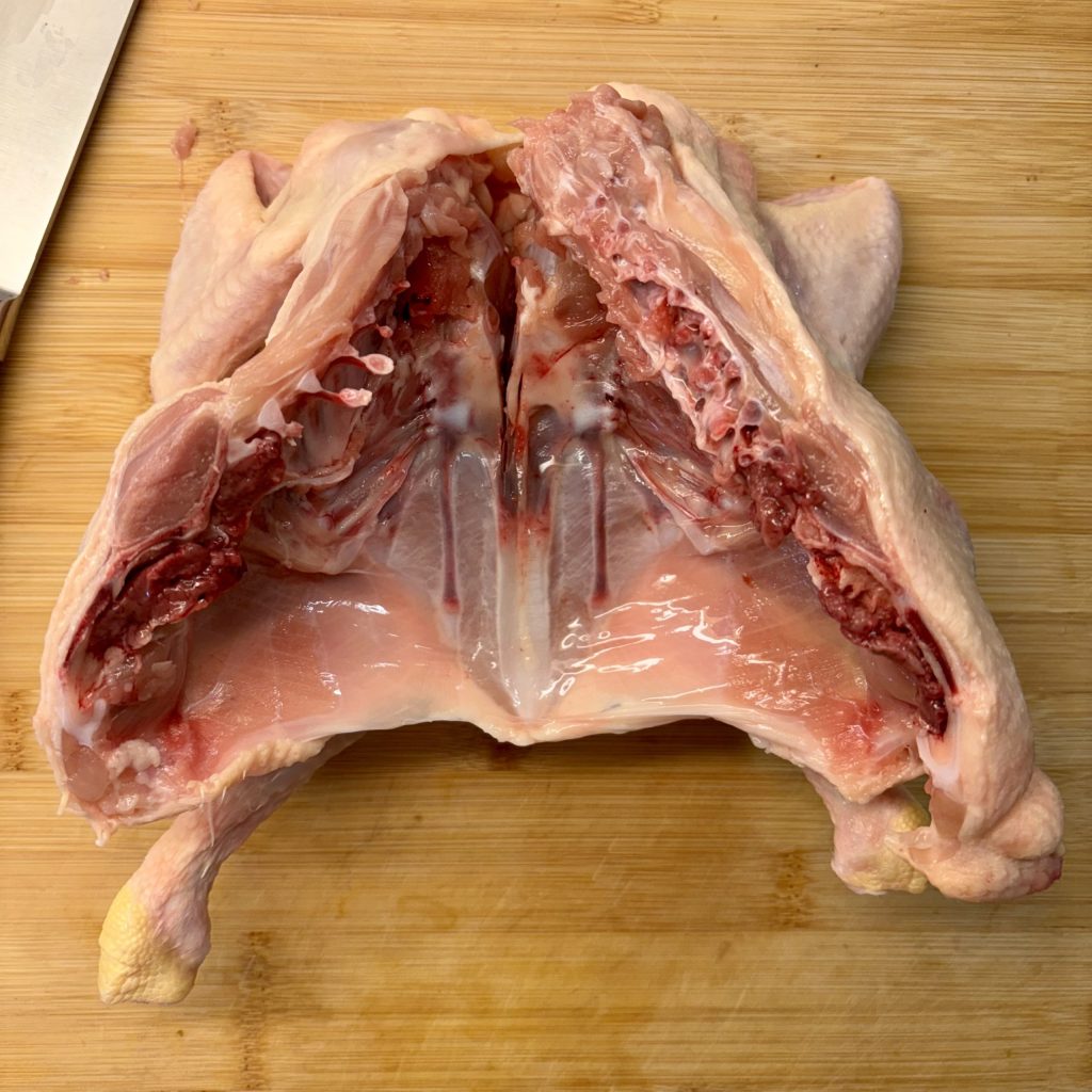 Aufgeschnittenes Hähnchen auf einem Holzbrett, bereit zum Würzen und Kochen.