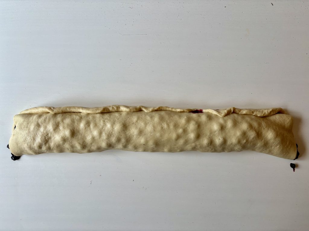 Ein ausgestreckter Teigstrang auf einem weißen Tisch.