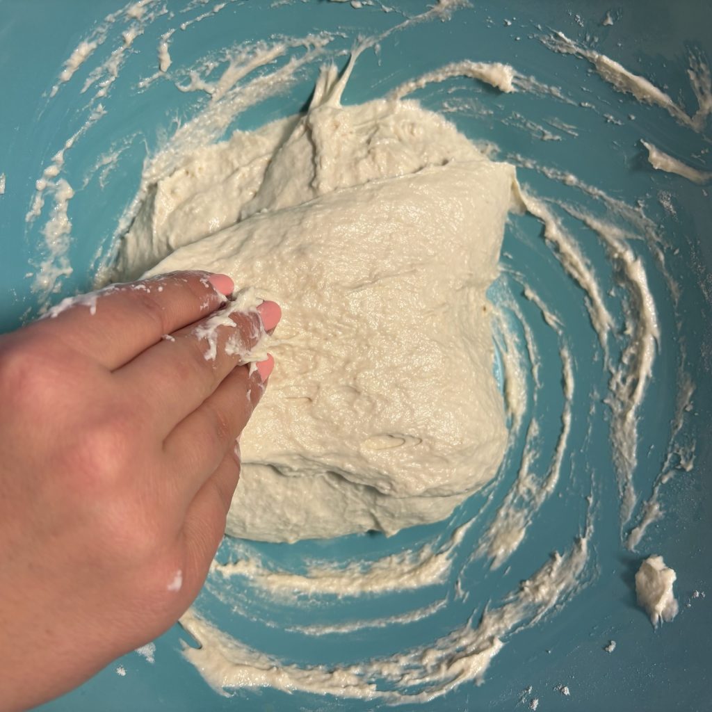 Eine Hand, die Teig in einer blauen Schüssel bearbeitet.