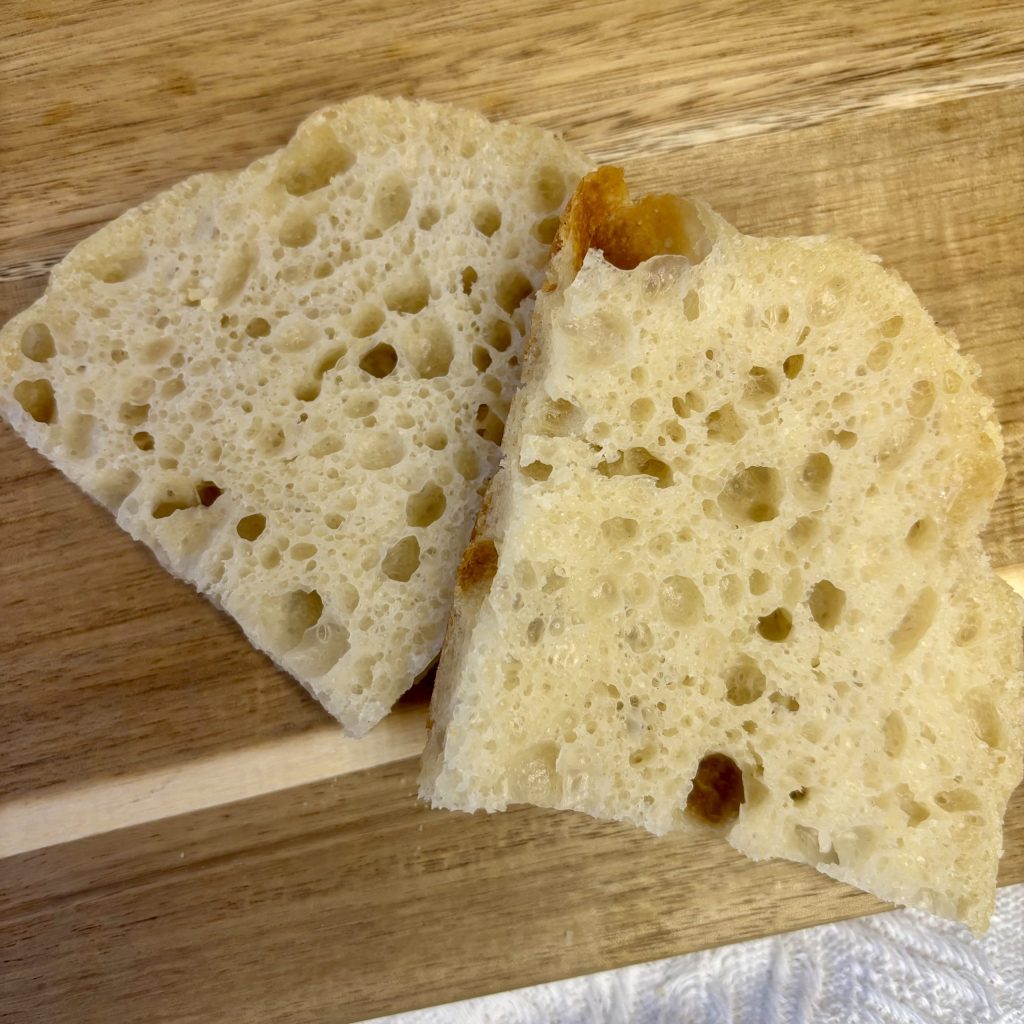 Zwei Stücke luftiges Brot auf einem Holzbrett, mit sichtbaren Löchern und einer goldenen Kruste.