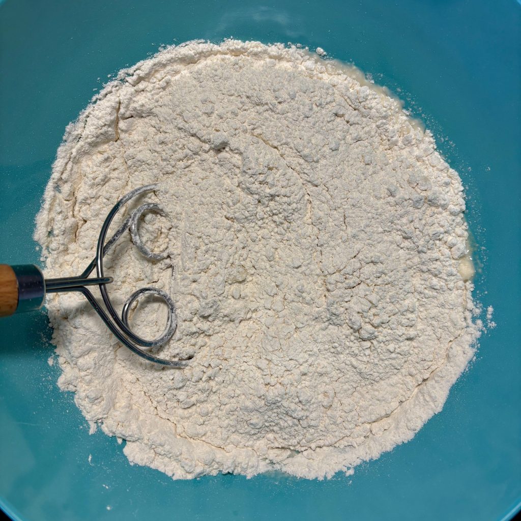 Eine Schüssel mit Mehl und einem Teigmischer mit Holzgriff.