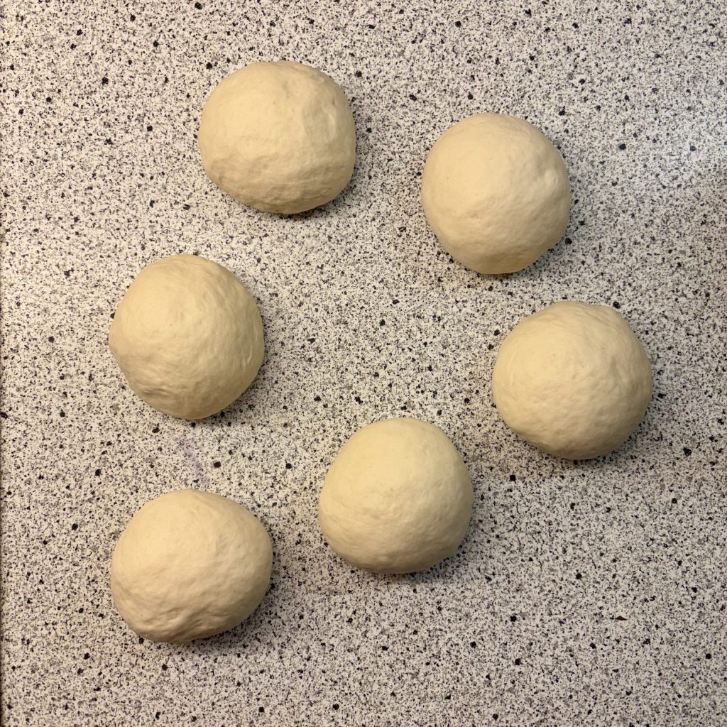 Sechs runde Teigkugeln auf einer grauen Arbeitsfläche.