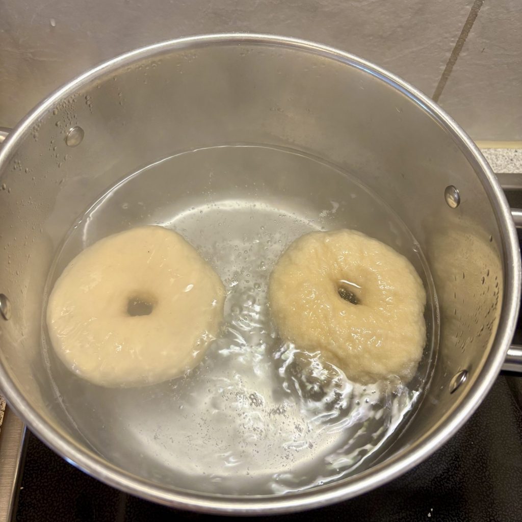 Zwei rohe Bagels, die in einem Topf mit sprudelndem Wasser kochen.