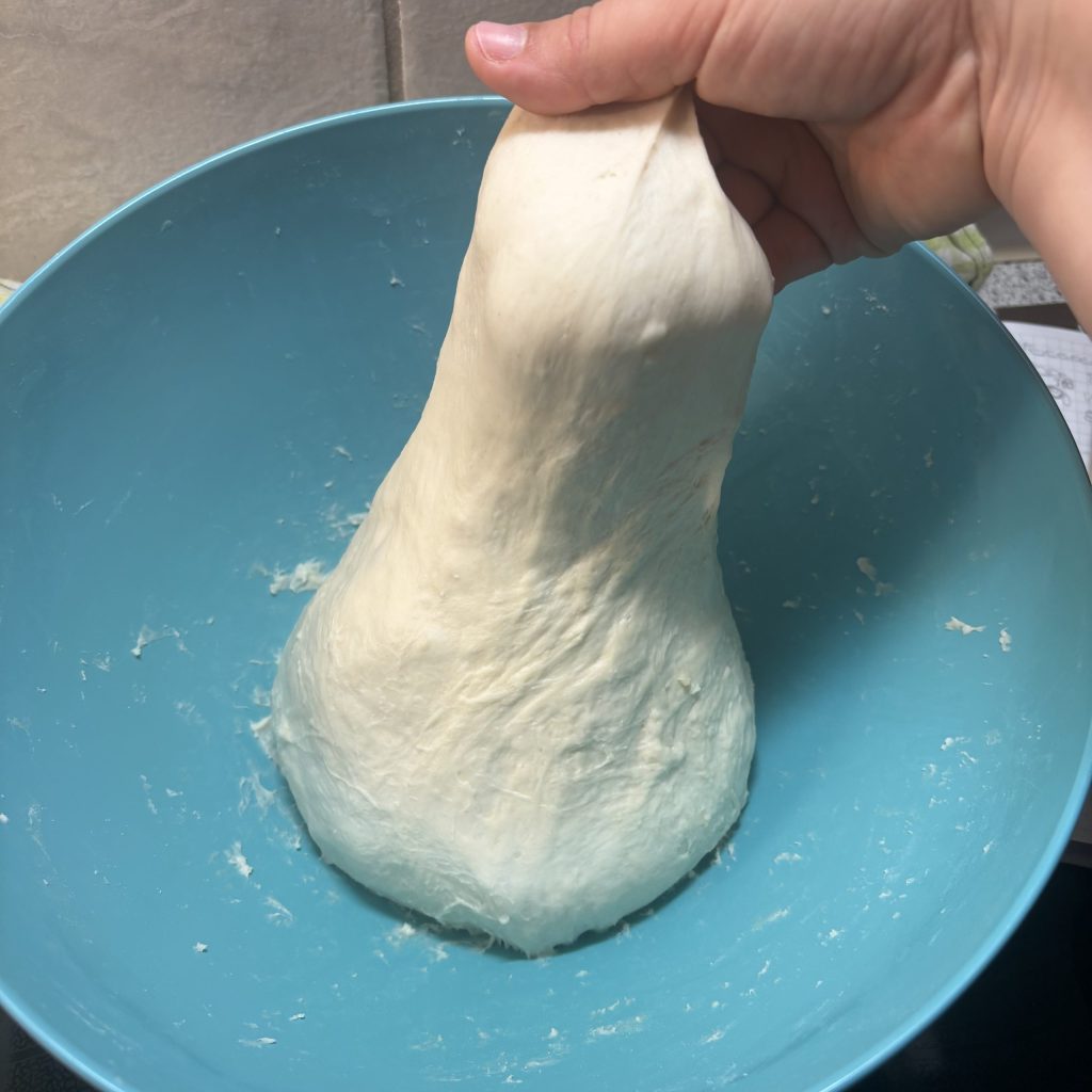Eine Hand zieht einen großen Klumpen Teig in einer blauen Schüssel.