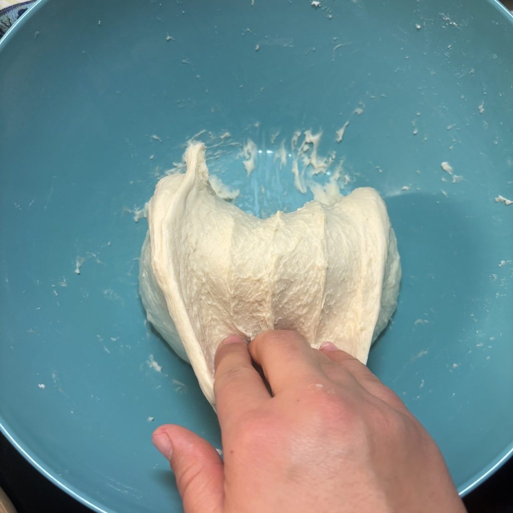 Eine Hand knetet Teig in einer blauen Schüssel.