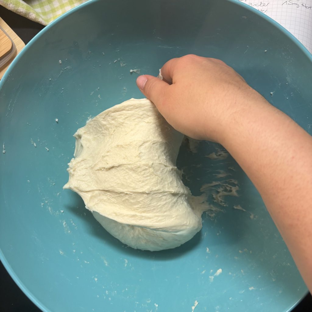 Eine Hand knetet einen Teig in einer blauen Schüssel.