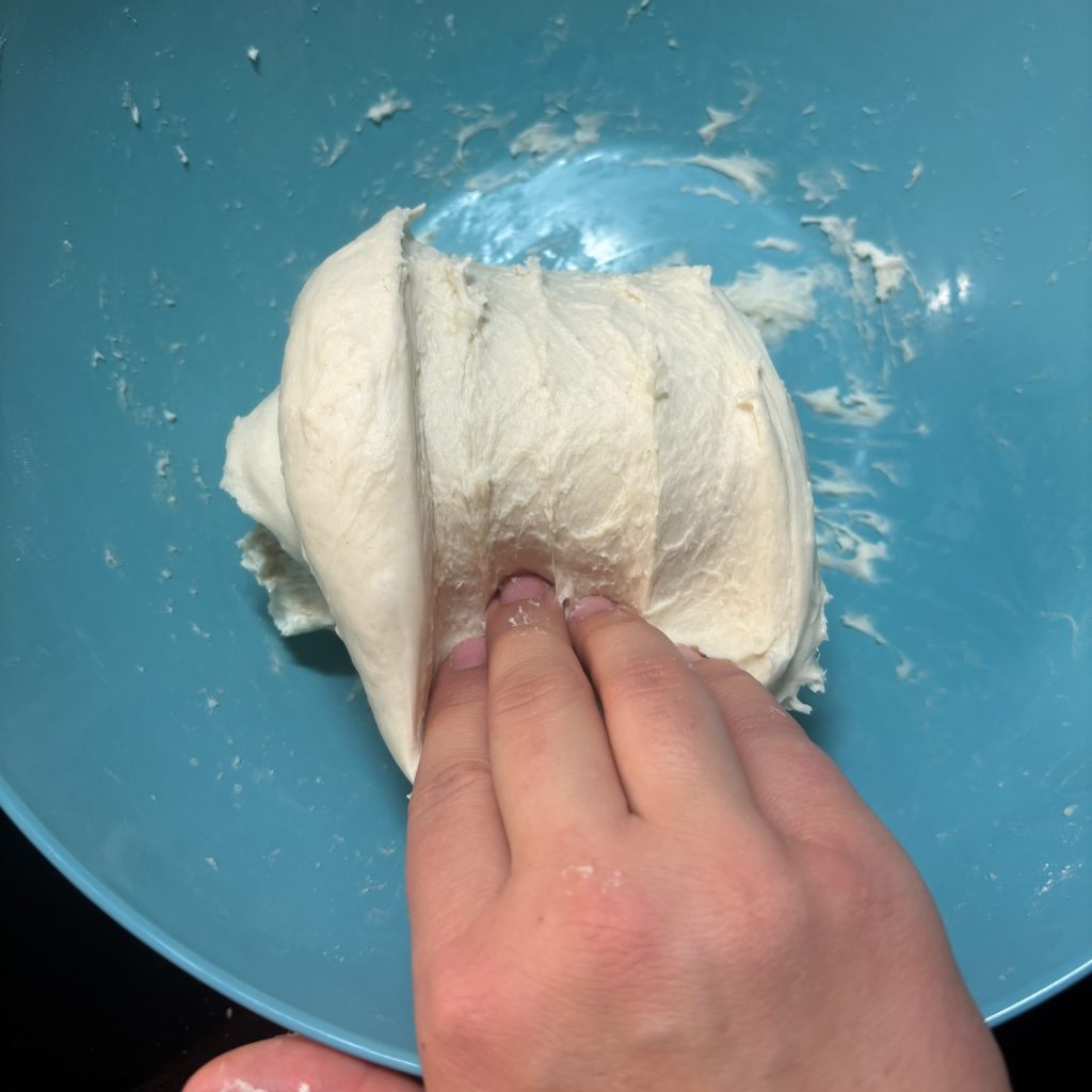 Eine Hand knetet einen Teig in einer blauen Schüssel.