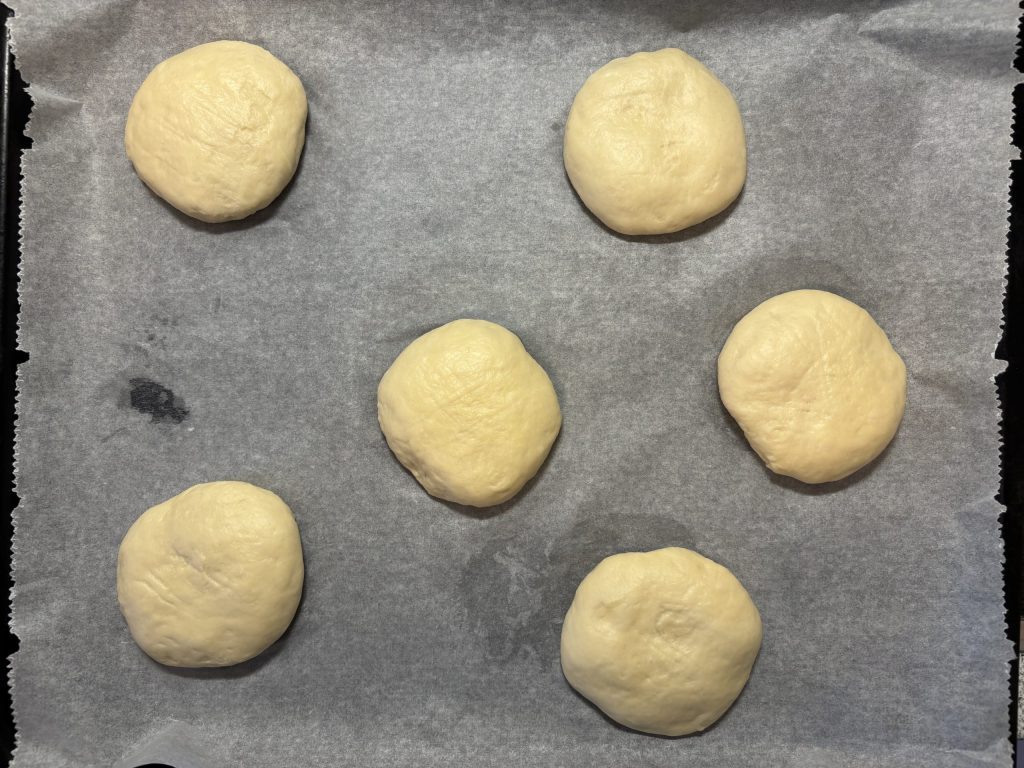 Flachgedrückte Sauerteig Burger Buns auf einem Backblech.
