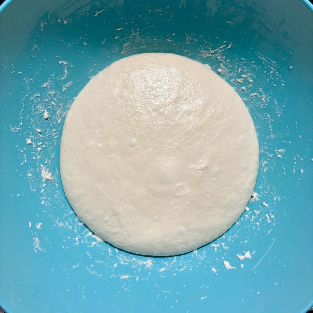 Kneteteig in einer blauen Schüssel, glatt und gleichmäßig auf der Oberfläche.
