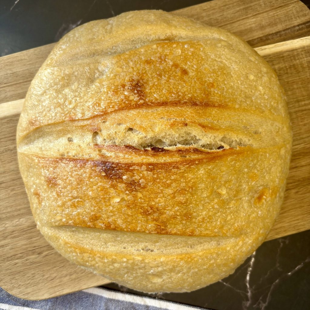 Ein frisch gebackenes Brot mit einer goldbraunen Kruste, auf einem Holzbrett präsentiert.
