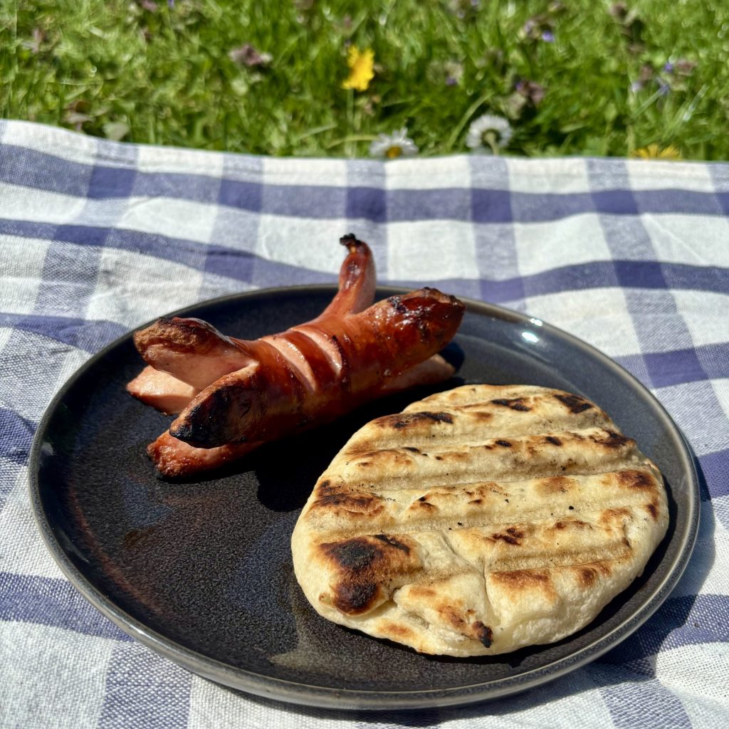 Gegrilltes Sauerteig Grillbrot mit Würstchen auf einem Teller im Freien
