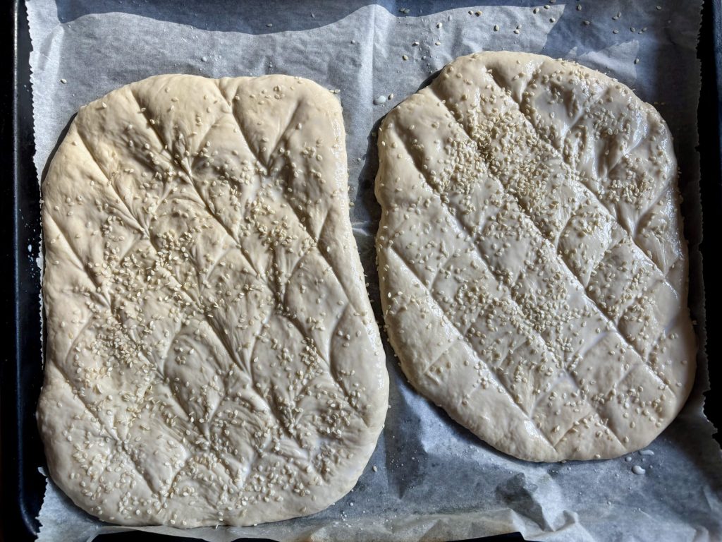 Sauerteig Fladenbrot roh geformt vor dem Backen, mit Sesam bestreut