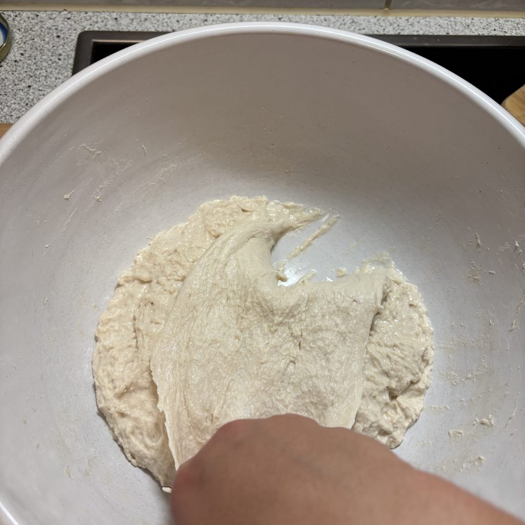 Klebriger Ciabatta Teig wird mit der Hand gedehnt