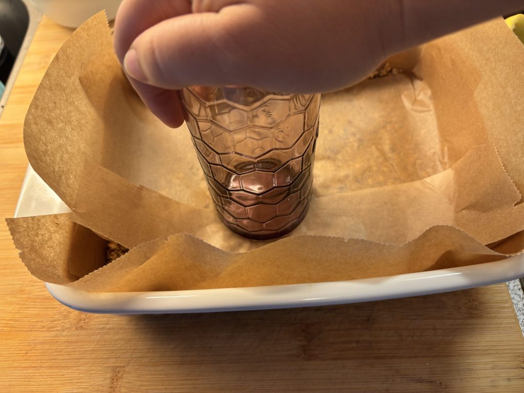 Müsliriegel Masse in einer Backform mit einem Glas festgedrückt
