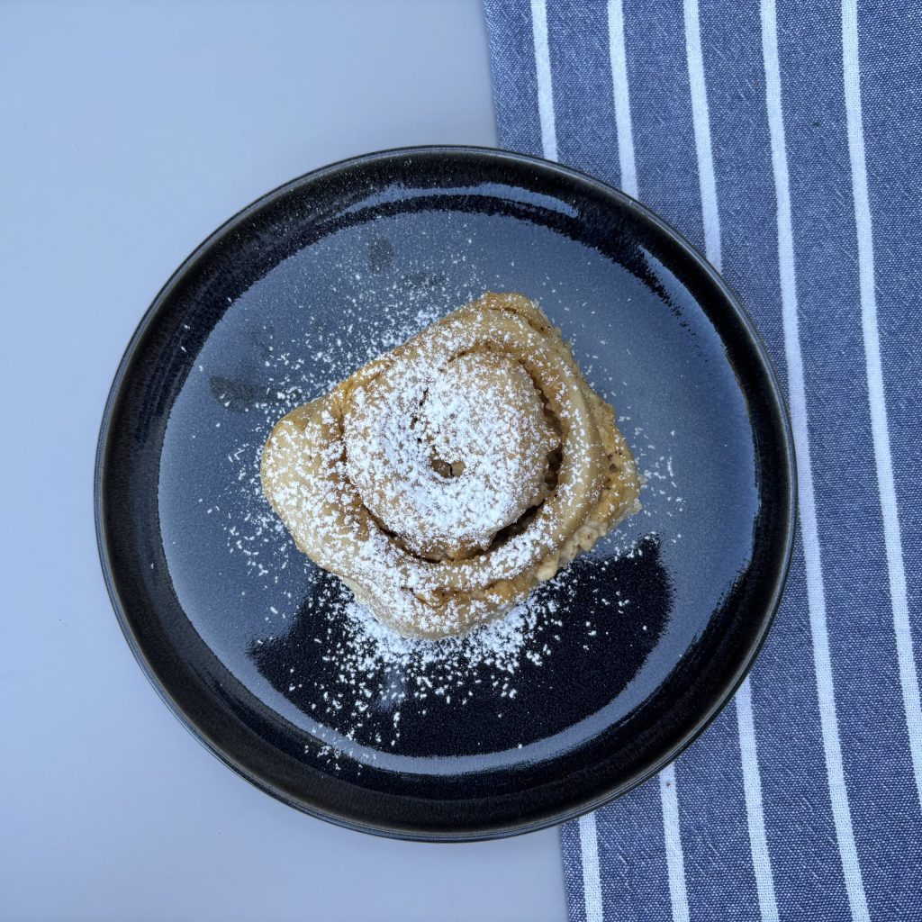 Puddingschnecke mit Sauerteig und Puderzucker auf schwarzem Teller