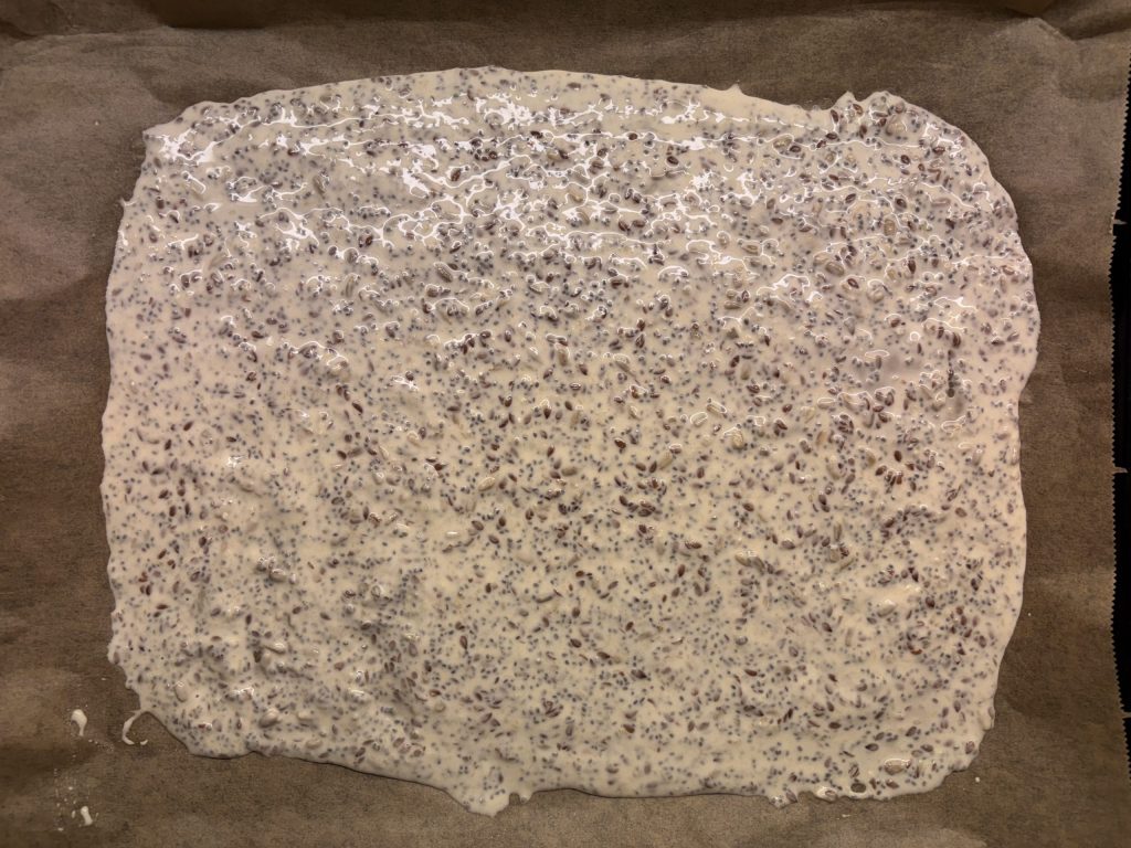 Dünn ausgestrichener Teig für Sauerteig Knäckebrot mit Saaten auf Backpapier