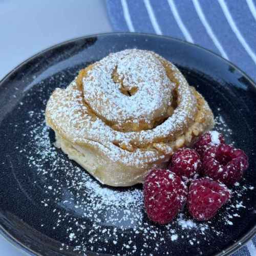 Alt-Text: Einzelne Puddingschnecke mit Sauerteig, Puderzucker und Himbeeren auf schwarzem Teller