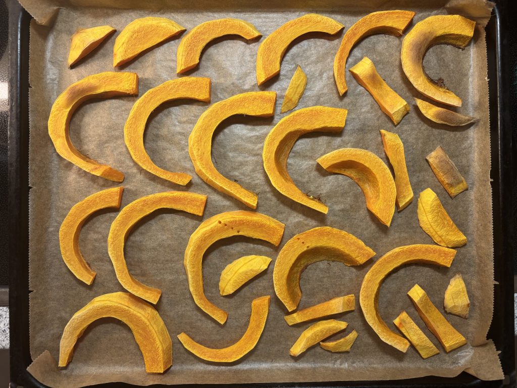 Geröstete Kürbisspalten auf einem mit Backpapier ausgelegten Backblech.