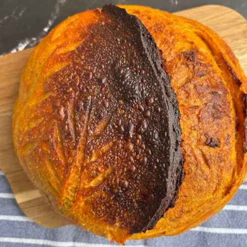 Kürbisbrot mit Sauerteig mit knuspriger Kruste und eingeschnittenem Blattmuster auf einem Holzbrett.