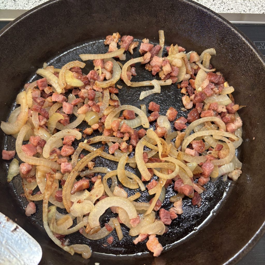 Speck und Zwiebeln in einer Pfanne am anbraten.